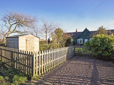 A fenced garden area with a wooden shed trees and a green house in the background at Periwinkle in Bamburgh