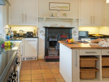 A kitchen with a wooden island countertop and baskets underneath a fireplace with white cabinets at The Villas No3 in Embleton