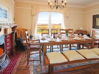 A dining room with wooden table and chairs a fireplace armchair and large window at The Villas No3 in Embleton