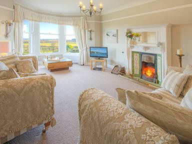 A living room with patterned sofas a fireplace a television and a window with a view at The Villas No3 in Embleton