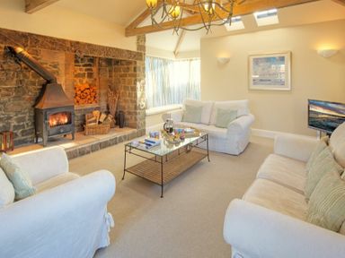 A living room with white sofas a stone fireplace and a glass coffee table at The Villas No3 in Embleton
