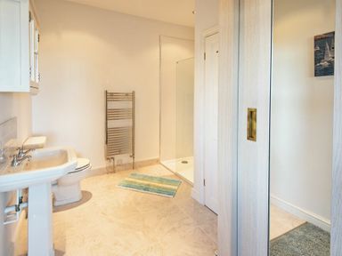 A bathroom with a sink, toilet, glass shower enclosure, towel radiator, and a rug at The Villas No3 in Embleton