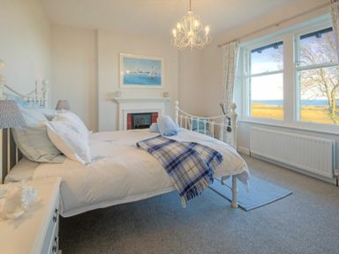 A bedroom with a double bed a fireplace a chandelier and a window with a sea view at The Villas No3 in Embleton