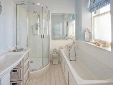 A bathroom with a shower, bathtub, sink with wicker drawers, and window at The Villas No3 in Embleton