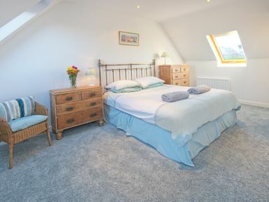 A bedroom with a double bed two wooden bedside chests lamps a wicker chair and a skylight window at The Villas No3 in Embleton