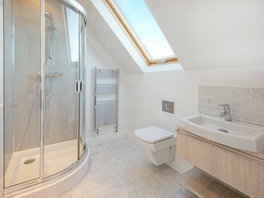 A bathroom with a curved glass shower cubicle a wall-mounted toilet a sink under a skylight window at The Villas No3 in Embleton