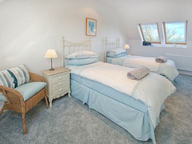 A bedroom with two single beds blue bed skirts and rolled towels on top with a nightstand lamp and wicker chair with cushions at The Villas No3 Embleton