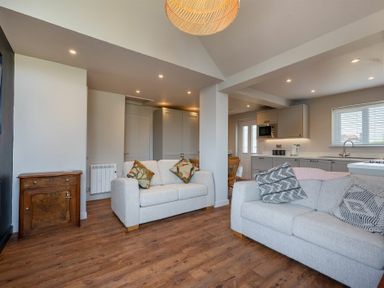 An open living room and kitchen with two beige sofas and wooden flooring at Castle View Bamburgh