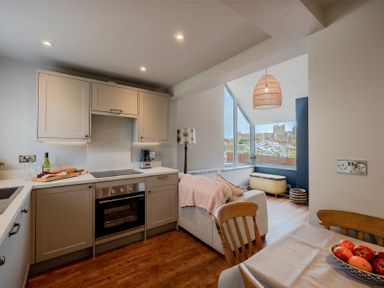 A kitchen with cabinets and an oven next to a dining table and a living area with a sofa and a large window at Castle View Bamburgh