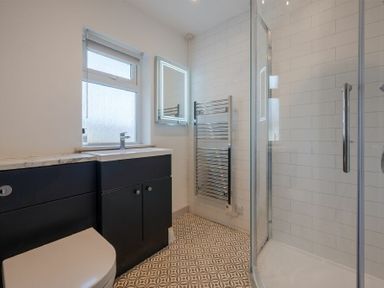 A bathroom with a toilet, sink, illuminated mirror, towel rack, and glass shower enclosure at Castle View Bamburgh