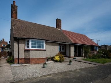 A bungalow with two chimneys a gravel front yard and a small garden area at Castle View Bamburgh