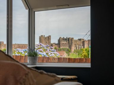 A window view showing a castle with flowering shrubs and part of a sofa at Castle View Bamburgh