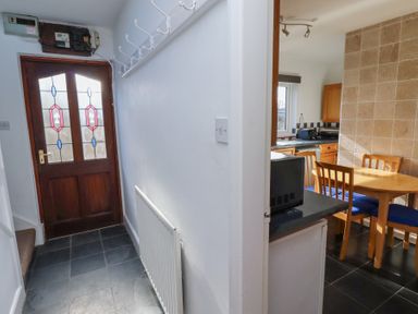A hallway with a wooden door and hooks on the wall next to a kitchen and dining area with a wooden table and chairs at St Marys Cottages No1 in Low Newton-by-the-Sea