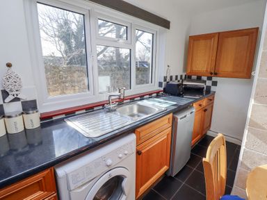 A kitchen with wooden cabinets a sink washing machine dishwasher and small appliances at St Marys Cottages No1 in Low Newton-by-the-Sea