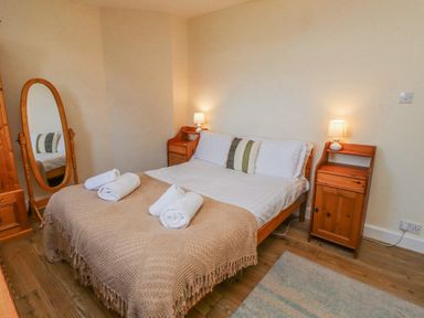 A bedroom with a double bed and two bedside tables with lamps and a full length mirror at St Marys Cottages No1 in Low Newton-by-the-Sea
