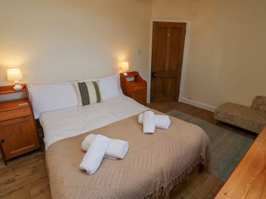 A bedroom with a double bed two bedside tables with lamps a chair and a wooden door at St Marys Cottages No1 in Low Newton-by-the-Sea