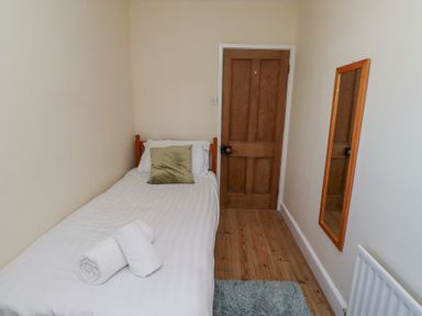 A small bedroom with a single bed a wooden door a wall mirror and a rug on a wooden floor at St Marys Cottages No1 in Low Newton-by-the-Sea