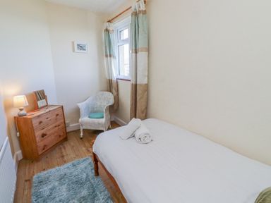 A bedroom with a single bed a wooden chest of drawers a wicker chair and a window at St Marys Cottages No1 in Low Newton-by-the-Sea