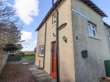 Exterior view of a corner cottage with a red door windows and mailbox at St Marys Cottages No1 in Low Newton-by-the-Sea