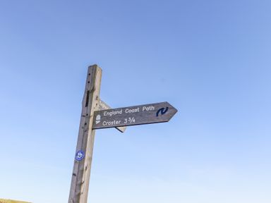 A wooden signpost showing directions for England Coast Path and Craster against a blue sky at St Marys Cottages No1 in Low Newton-by-the-Sea