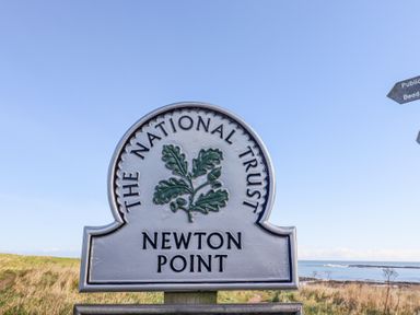 A sign for The National Trust Newton Point on a grassy coastline with the sea in the background at St Marys Cottages No1 in Low Newton-by-the-Sea