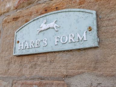 A wall-mounted sign with a hare figure and the text Hares Form on a stone wall at Hares Form in Seahouses