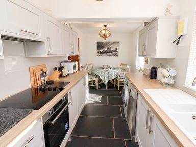 A kitchen with white cabinets wooden countertops dining table with chairs and black and white wall art at Hares Form in Seahouses