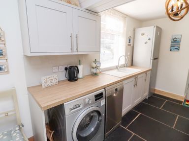 A kitchen with washing machine dishwasher refrigerator and sink with window at Hares Form in Seahouses