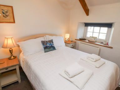 A bedroom with a double bed two bedside tables with lamps a window and folded towels on the bed at Hares Form in Seahouses