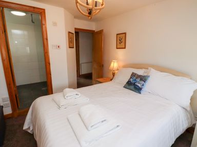 A bedroom with a double bed with white linens and folded towels bedside lamp and two framed pictures on the wall at Hares Form in Seahouses
