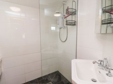 A bathroom with a shower area with a wall-mounted shower unit a sink with a faucet and a mirror above at Hares Form in Seahouses