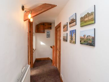 A hallway with a wooden door and wall-mounted light fixture and photos on the wall at Hares Form in Seahouses