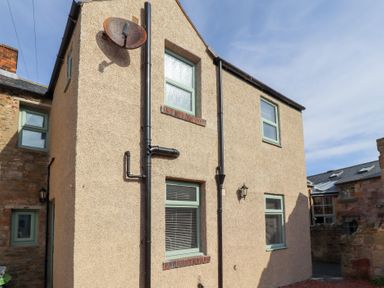 An exterior view of a beige stucco house with green framed windows and black rain gutters at Hares Form in Seahouses
