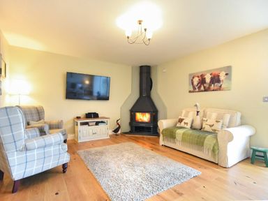 A living room with a fireplace plaid armchairs a white sofa and a flat screen TV at The Pepper Pot in Warkworth