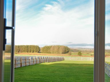 A view of a fenced green field and trees seen through an open window at The Pepper Pot in Warkworth