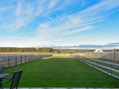 A long fenced grassy backyard with patio chairs and a table under a blue sky at The Pepper Pot in Warkworth