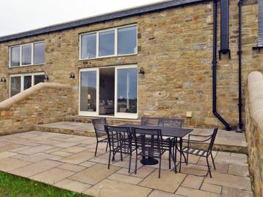 An outdoor patio with a black metal table and six chairs outside a stone house at The Pepper Pot in Warkworth