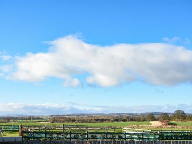 A rural landscape with fields trees fences and a cloudy blue sky at The Pepper Pot in Warkworth