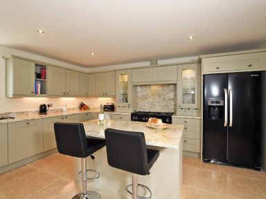 A kitchen with light cabinets a black refrigerator an island with two black stools and various kitchen appliances at The Pepper Pot in Warkworth
