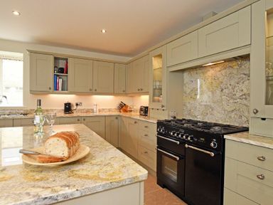 A kitchen with beige cabinets granite countertops a black stove sliced bread on a plate with a knife and two wine glasses at The Pepper Pot in Warkworth