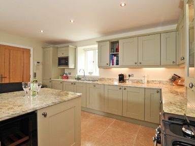 A kitchen with beige cabinets a marble countertop a bottle of wine and glasses on an island at The Pepper Pot in Warkworth