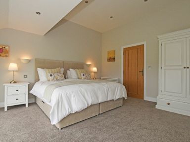 A bedroom with a double bed two bedside tables with lamps a wooden door and a white wardrobe at The Pepper Pot in Warkworth
