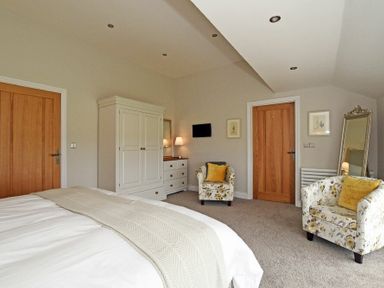 A bedroom with a bed a white wardrobe two floral armchairs a mirror and two wooden doors at The Pepper Pot in Warkworth