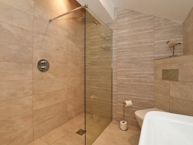 A shower area with a glass partition a toilet with a toilet paper holder and a decorative bird figure on a shelf in a bathroom at The Pepper Pot in Warkworth