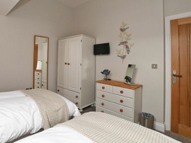 A bedroom with two beds a white wardrobe a chest of drawers with a mirror and a wall-mounted television at The Pepper Pot in Warkworth
