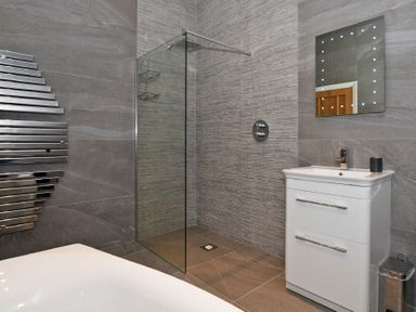 A bathroom with a walk-in shower, a white sink vanity, a mirror with lights, and a towel radiator at The Pepper Pot in Warkworth