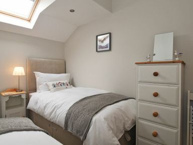 A bedroom with two single beds a bedside table with a lamp a chest of drawers with a mirror and wall art at The Pepper Pot in Warkworth