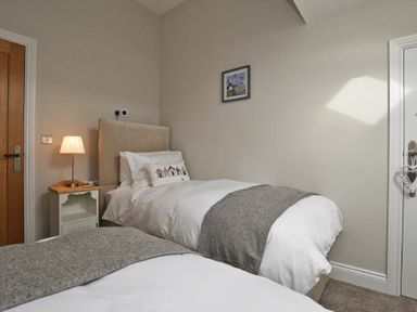 A bedroom with two single beds a bedside table with a lamp a wooden door and a picture on the wall at The Pepper Pot in Warkworth