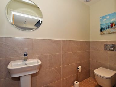 A bathroom with a sink round mirror toilet and a painting on the wall at The Pepper Pot in Warkworth
