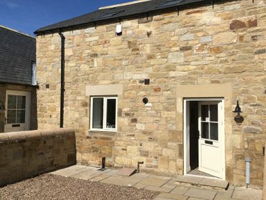 Stone exterior wall with a door and window and a small stone patio with gravel at The Pepper Pot in Warkworth